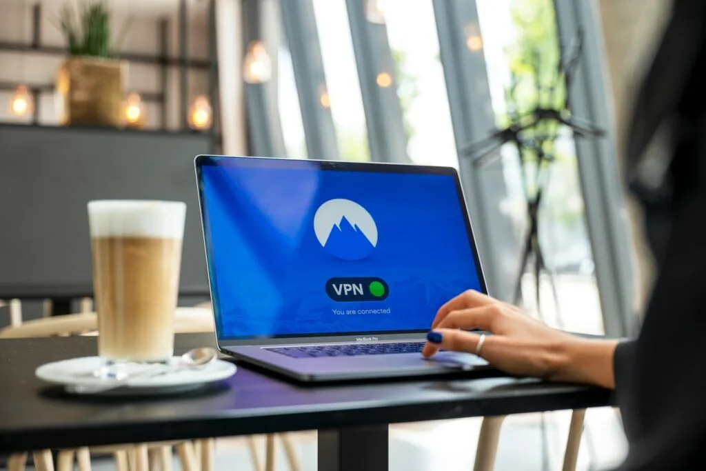 Eine Person sitzt vor dem Schreibtisch., vor ihm ein Laptop  mit einem NordVPN Schriftzug und danaben ein Latte Machiatto