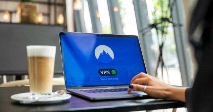 Eine Person sitzt vor dem Schreibtisch., vor ihm ein Laptop mit einem NordVPN Schriftzug und danaben ein Latte Machiatto