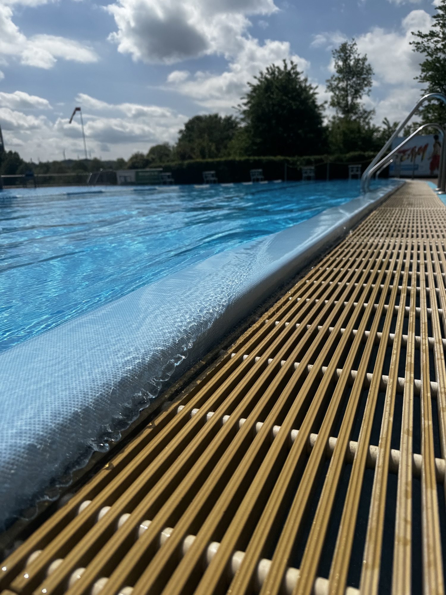 Sommerlicher Swimmingpool mit blauem Wasser, Pooldeck und Leiter im Grünen
